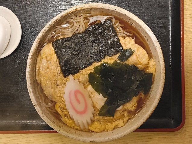 『琴富貴』の「玉子とじそば」でランチ。この「玉子とじそば」、なぜか食べたい蕎麦なのだが、特徴はやはりあのふわふわとした黄色い溶き玉子だろう。 まるで敷き布団のように一面を覆う玉子を背景に、なるとの鮮やかな白とピンク、海苔とわかめの深緑が実によく映える。うまいのだよ（笑）。（琴富貴：墨田区吾妻橋1）