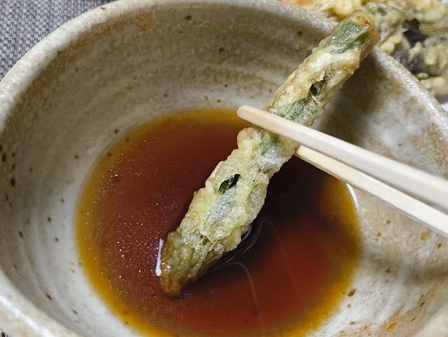 汁をつけてアスパラの天ぷらを食べる