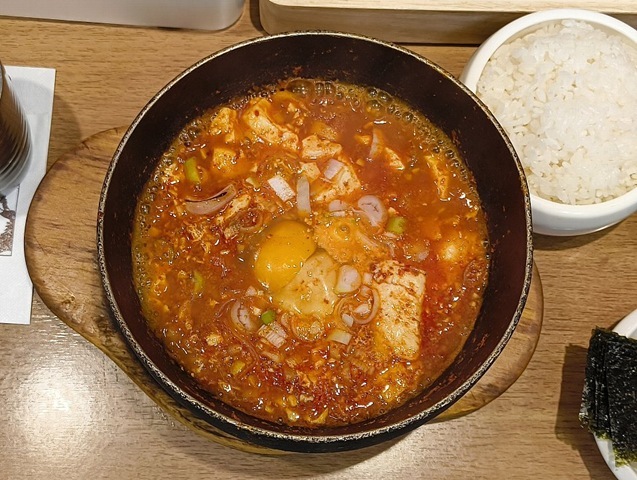 『妻家房 松屋浅草店』の「スンドゥブチゲ」でランチ。ご飯を「スンドゥプチゲ」にひたしで口の中に放り込む。本音を言えばご飯をスープへ丸ごと投入して豪快に喰らいつきたいところだが、そこはグッと我慢。しかし、これがうまいのだよ（笑）。（妻家房 松屋浅草店：花川戸一丁目）