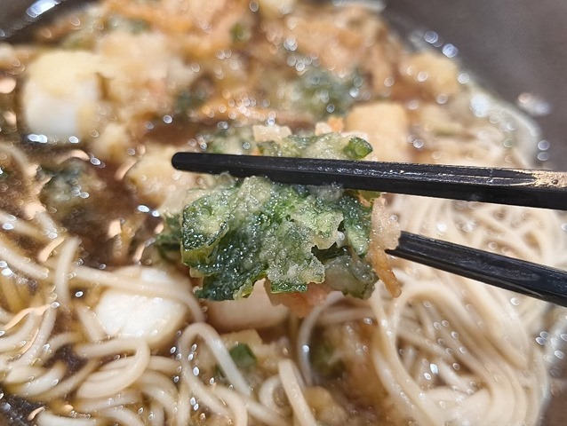 春菊のかけらを箸でつまみ口にはこぶ