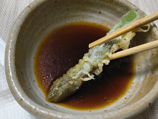 蕎麦汁をつけてアスパラの天ぷらを食べる