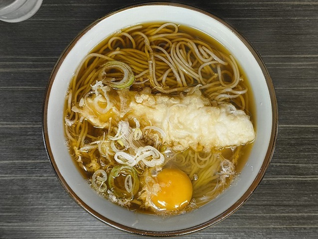 『文殊 浅草店』で「イカ天そば」と「生たまご」でランチ。「生たまご」を「イカ天」の無い片側に広げれば、イカの「白」と黄身の「黄」が見事なコントラストを描き出す。 その「生たまご」を纏った蕎麦をズルズルと手繰れば、いやはや、もう堪らない。 うまいのだよ（笑）。（文殊 浅草店：浅草一丁目：浅草地下街）