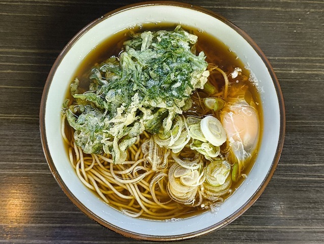 「文殊」の「春菊天そば」＋「生たまご」でランチ。「春菊天」を「汁」に浸すのだが、 香りは益々ひろがるのだ。ここで「たまご」を崩して「春菊」の緑と「たまご」の黄色の対比を楽しむ。そして確信するのだ。 これは絶対にうまいのだと（笑）。（文殊 浅草店：浅草一丁目：浅草地下街）