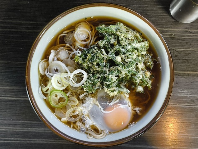 『文殊 浅草店』で、私的な無形重要文化財である「春菊天そば」に「生たまご」を落としてのランチ。途中で「生たまご」を「春菊天」の無い片側に広げれば、春菊の「緑」と黄身の「黄」が見事なコントラストを描き出す。 その「生たまご」を纏った蕎麦をズルズルと手繰れば、いやはや、もう堪らないのだ（笑）。（文殊浅草店：浅草一丁目：浅草地下街）