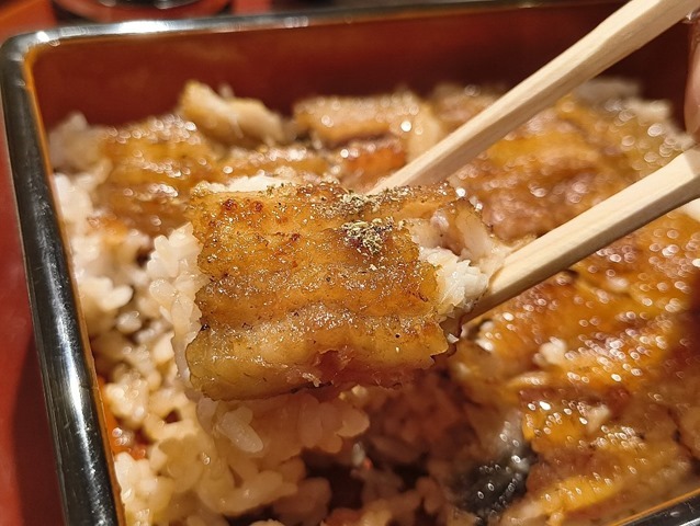 山椒をふってうなぎ重を食べる